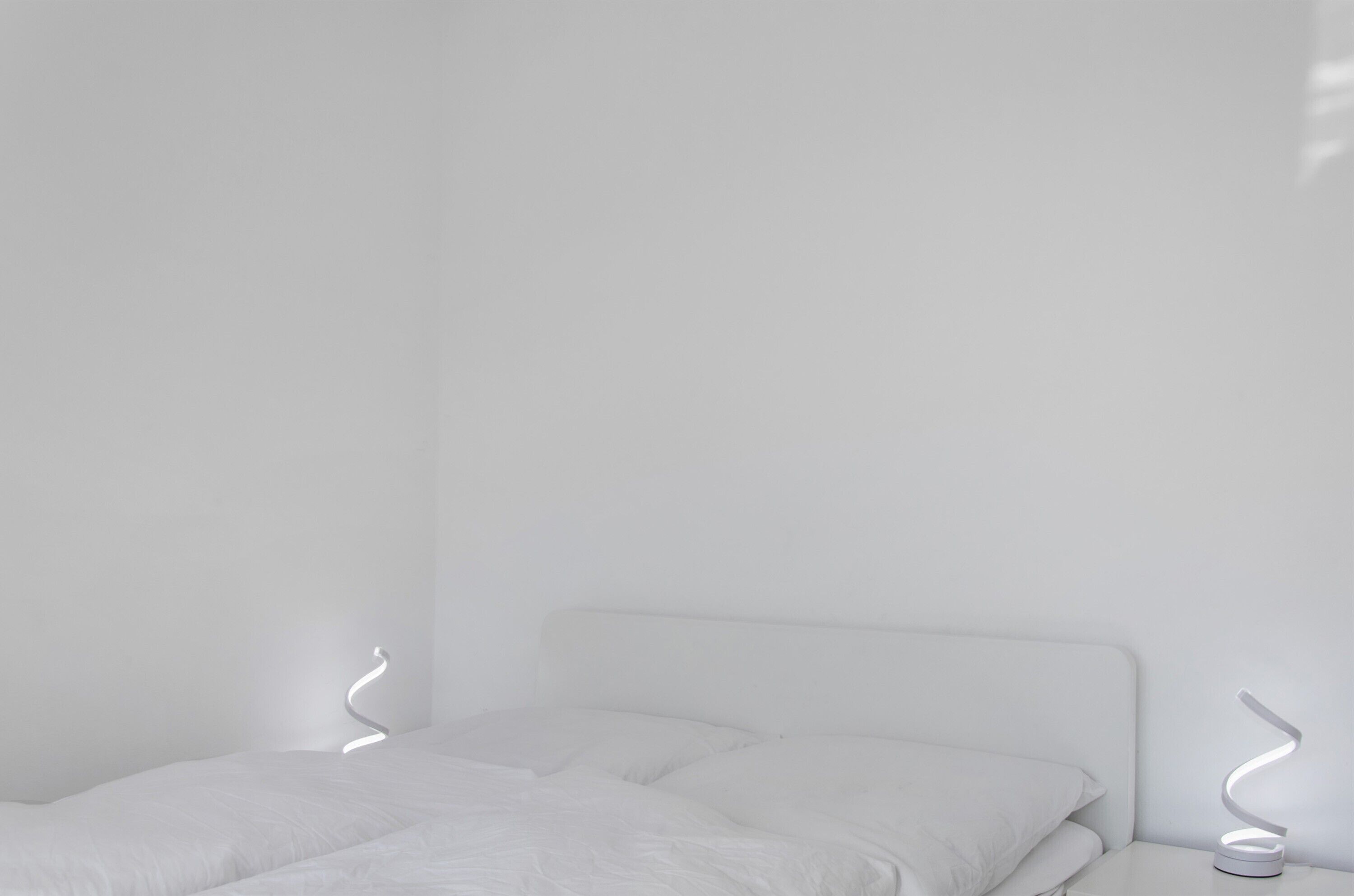 Una camera da letto dal design minimalista con un letto, pareti bianche e un moderno apparecchio di illuminazione.