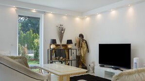 Ein Wohnzimmer mit einer Couch, einem Fernseher, einer Statue und einem Tisch mit Lampen.