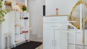 Ein Zimmer mit einem weißen Schrank, einem Regal mit einem Stofftier, einer Pflanze und einem Spiegel mit goldener Rahmung.
