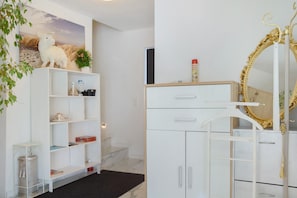 Une pièce avec une armoire blanche, une étagère sur laquelle est posé un animal en peluche, une plante et un miroir avec un cadre doré.