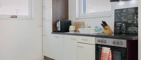 Una cocina con armarios blancos, una cafetera, un tostador, un bloque de cuchillos y una estufa.
