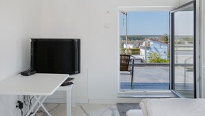 Ein Zimmer mit Fernseher auf einem weißen Schreibtisch, einem Bett und einer Glastür zu einem Balkon.