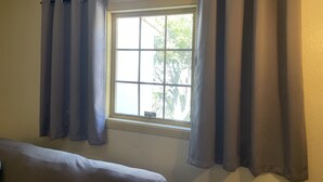 Een kamer met raam, gordijnen en een bed.