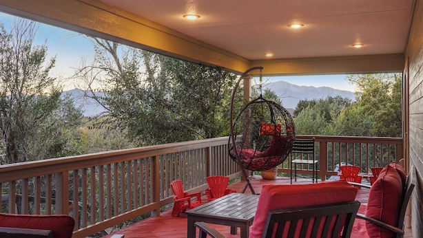 A covered outdoor deck with red chairs and a table, overlooking a mountainous landscape.