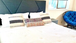 A neatly made bed with patterned pillows, a blue chair, and framed artwork on the wall.