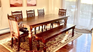 A dining area with a wooden table and chairs, a patterned rug, and two abstract paintings on the wall.