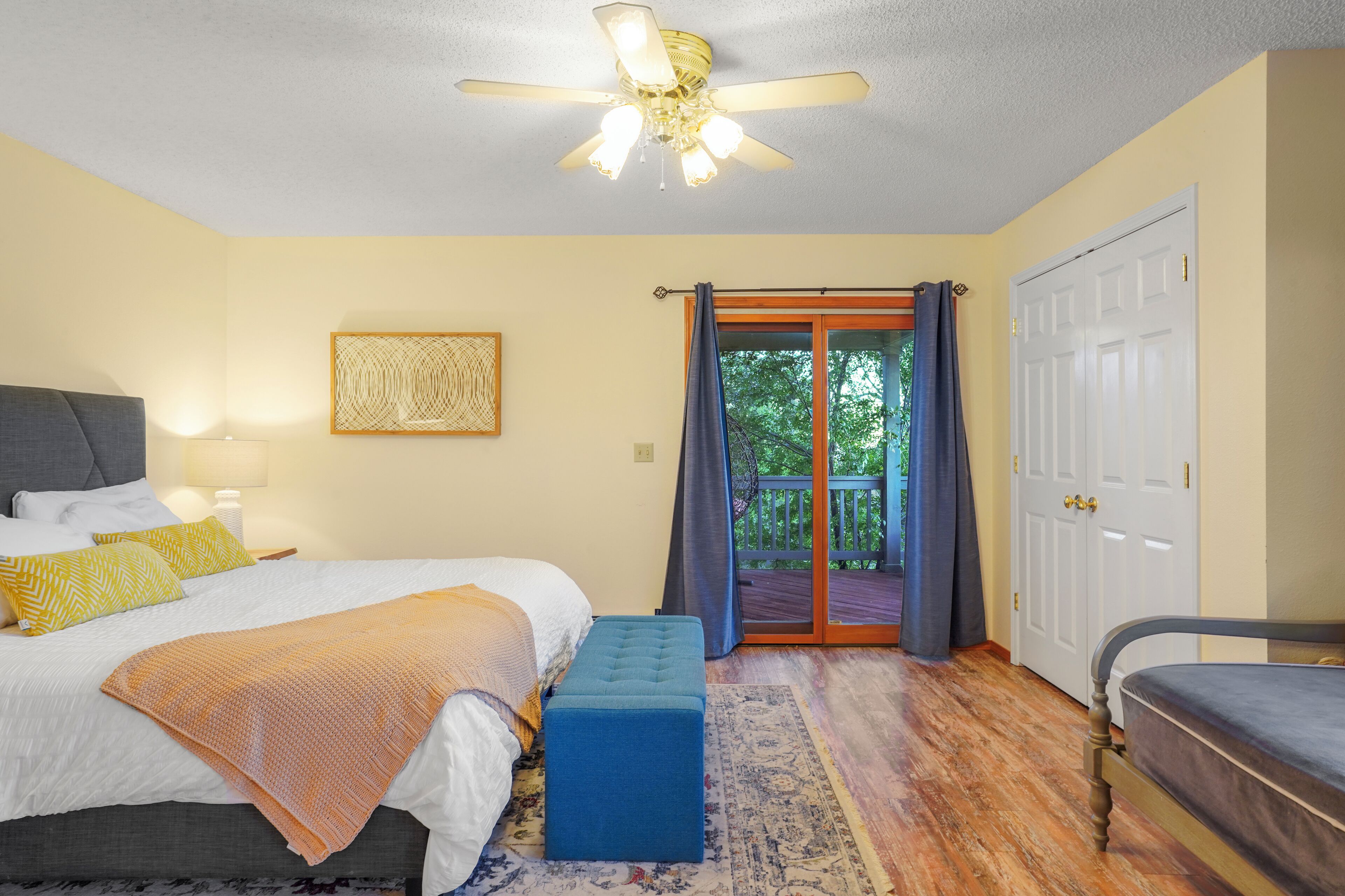 Ein Schlafzimmer mit Bett, einer Bank, einem Deckenventilator, einer Tür und Blick ins Freie.