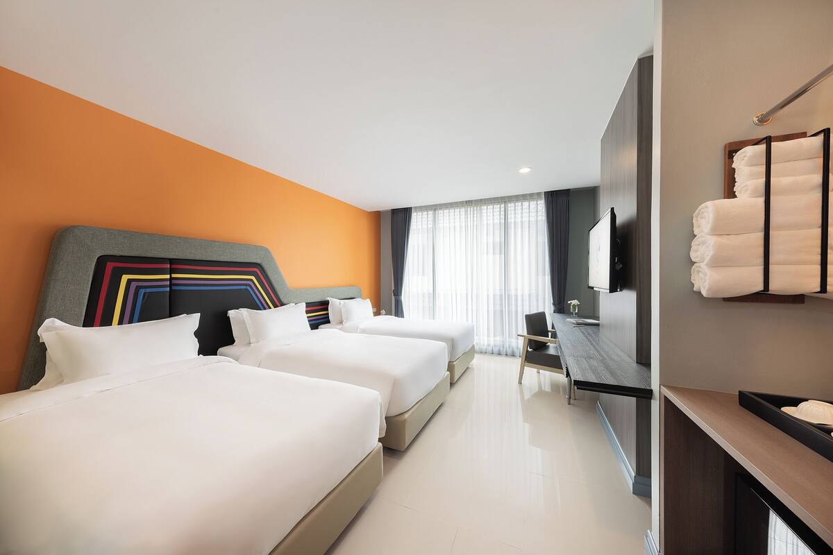 A hotel room with two beds, a desk, a TV, and a bathroom with a towel rack.
