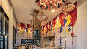 A modern dining area with high ceilings, patterned ceiling decorations, and a kitchen in the background. - Hotel Selene Chiang Rai (Chiang Rai)