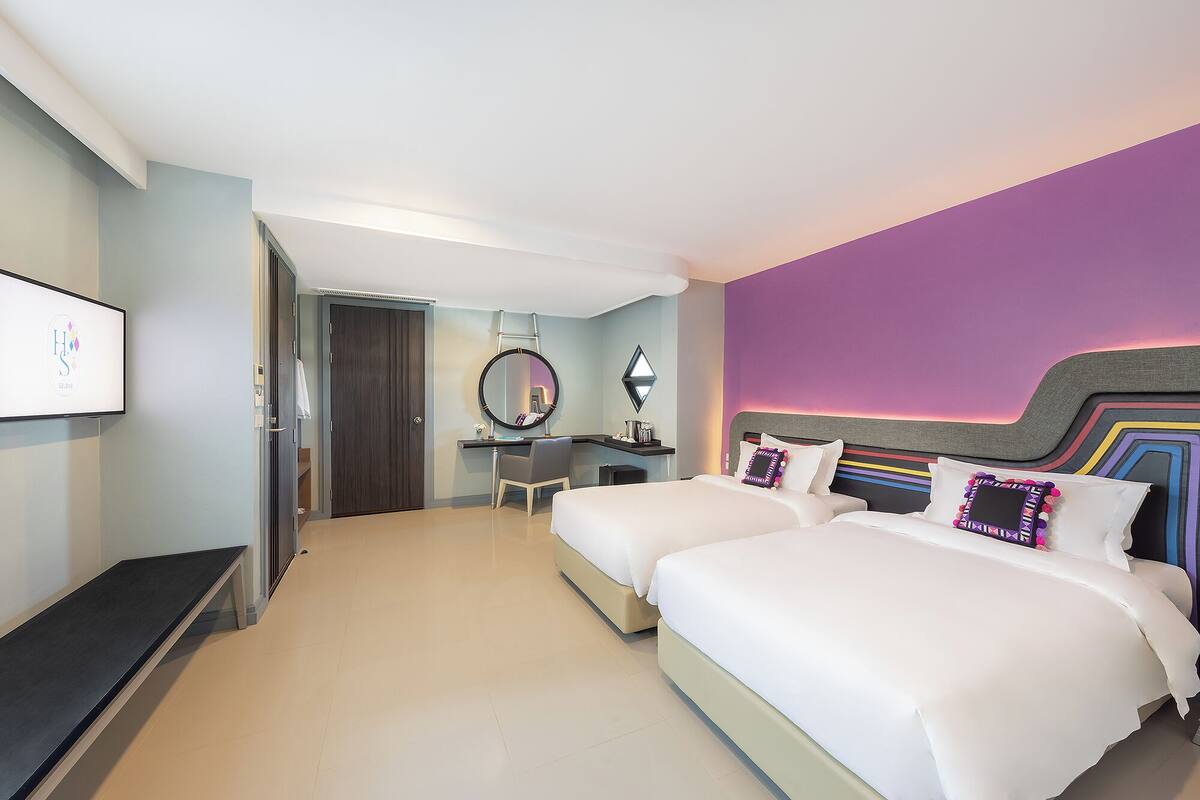 A hotel room with two beds, a desk, a chair, a TV, and a bathroom door.