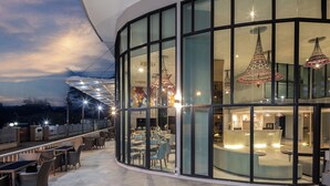 A modern building with large glass windows, outdoor seating, and decorative hanging lights. - Hotel Selene Chiang Rai (Chiang Rai)