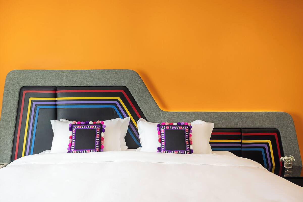A bed with a colorful headboard, white bedding, and decorative pillows.