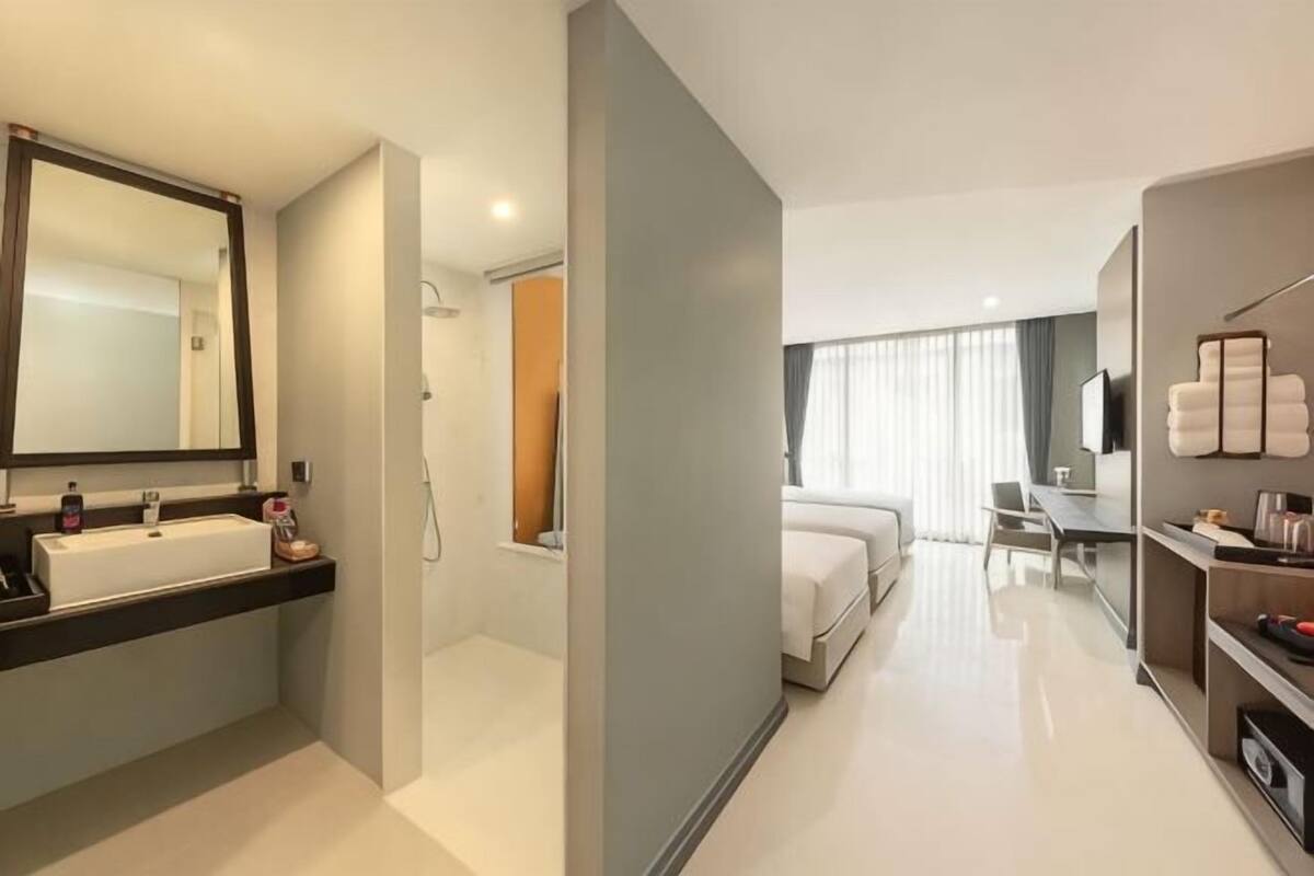 A modern hotel room with a bathroom, a bed, a desk, and a TV.