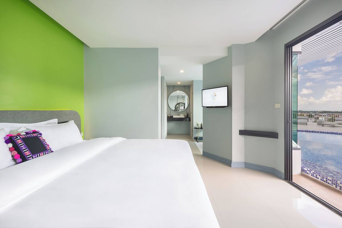 A modern hotel room with a large bed, a television, and a view of a pool.