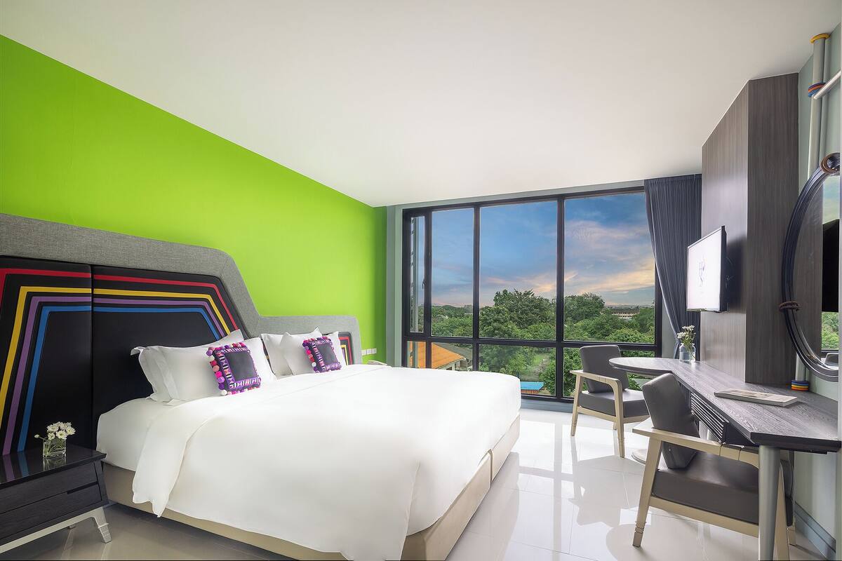 A modern hotel room with a large bed, a desk, and a view of the outdoors.