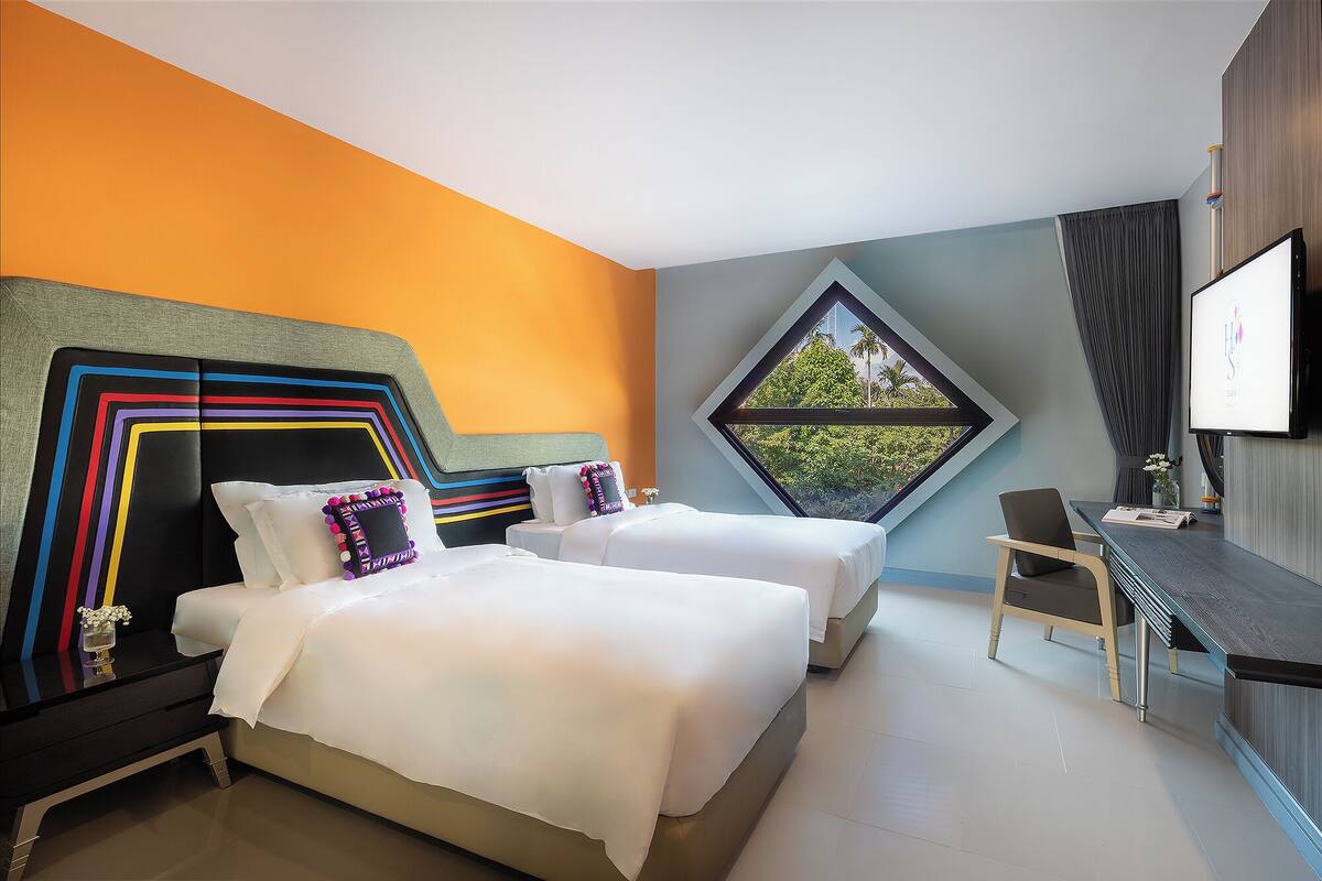 A hotel room with two beds, a desk, and a large window.