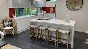 Una cocina moderna con una isla central, taburetes de bar, un reloj grande y una ventana con follaje verde en el exterior.