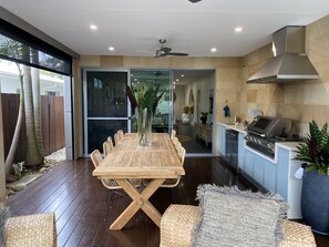 A modern kitchen with a wooden dining table, built-in appliances, and a sliding glass door leading to a patio area. - The Palm - Beachside Home with Heated Pool, Cinema & Games Room (Mudjimba)