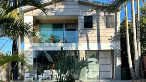 Una casa moderna de dos pisos con fachada de vidrio, piscina y palmeras.