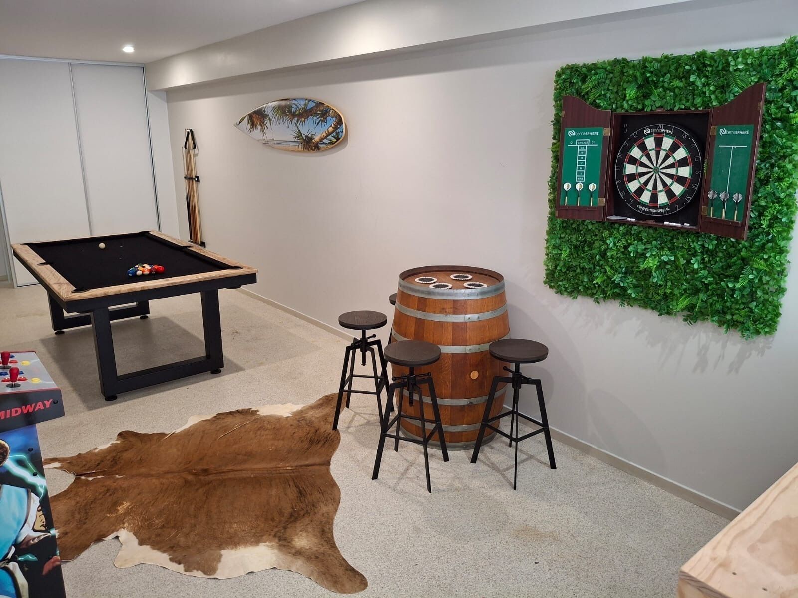 Une pièce équipée d’une table de billard, d’un jeu de fléchettes, d’un ensemble de tabourets de bar et d’un tapis en peau de vache.