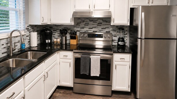 Una cocina moderna con electrodomésticos de acero inoxidable, armarios blancos y salpicadero de azulejos.