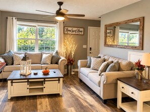 A cozy living room with two sofas, a coffee table, a side table, a ceiling fan, and a window with curtains. - Amazing Beds!-2 miles to Dollywood-The Island-Tanger (Sevierville)
