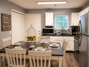 Una cocina moderna con armarios blancos, un refrigerador de acero inoxidable y un comedor preparado para seis personas con sillas y una mesa blancos.