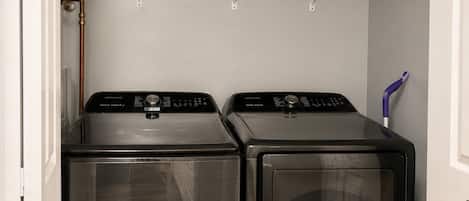 A laundry area with two front-loading washing machines and a shelf above holding folded clothes.