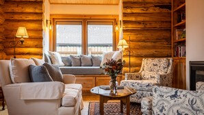 Interior acogedor de una cabaña de troncos con sofá, sillón y una pequeña mesa con un florero.