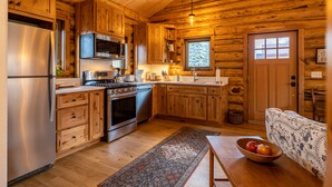 Cocina de cabaña de madera con refrigerador, estufa, microondas, pileta y armarios de madera.