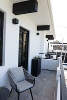 A balcony with a chair, a potted plant, and a black rectangular object on the wall.