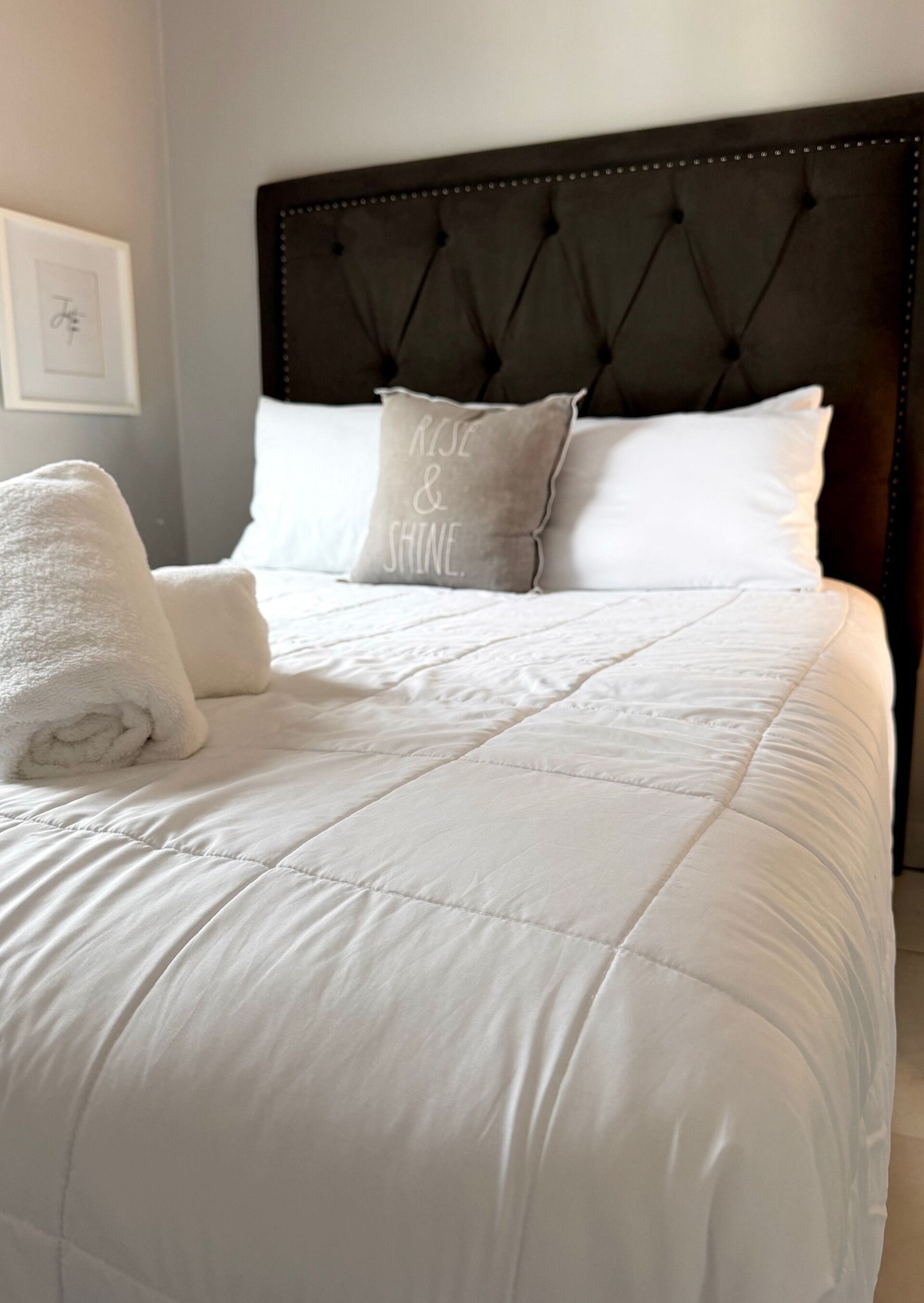 A neatly made bed with a white duvet, two pillows, and a rolled white towel.
