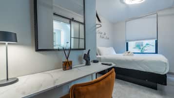 A modern hotel room with a bed, a desk with a lamp, a chair, and a large mirror.
