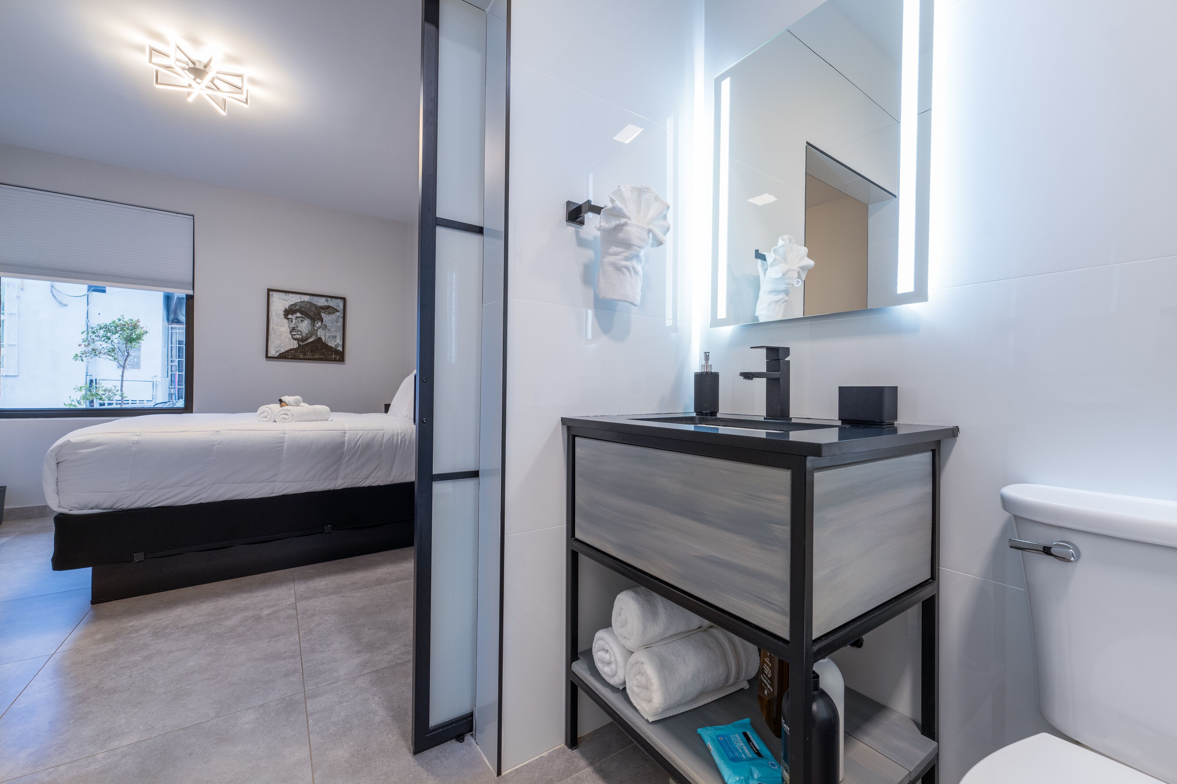 A modern hotel room with a bed, a bathroom with a mirror, and a toilet.