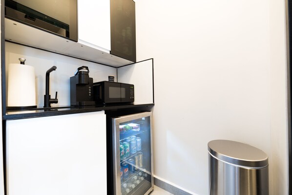 Una kitchenette compacta con microondas, cafetera y un refrigerador pequeño lleno de bebidas.