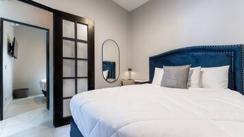 Une chambre d’hôtel moderne avec un grand lit, une table de chevet avec une lampe, un miroir et une vue sur la salle de bain.