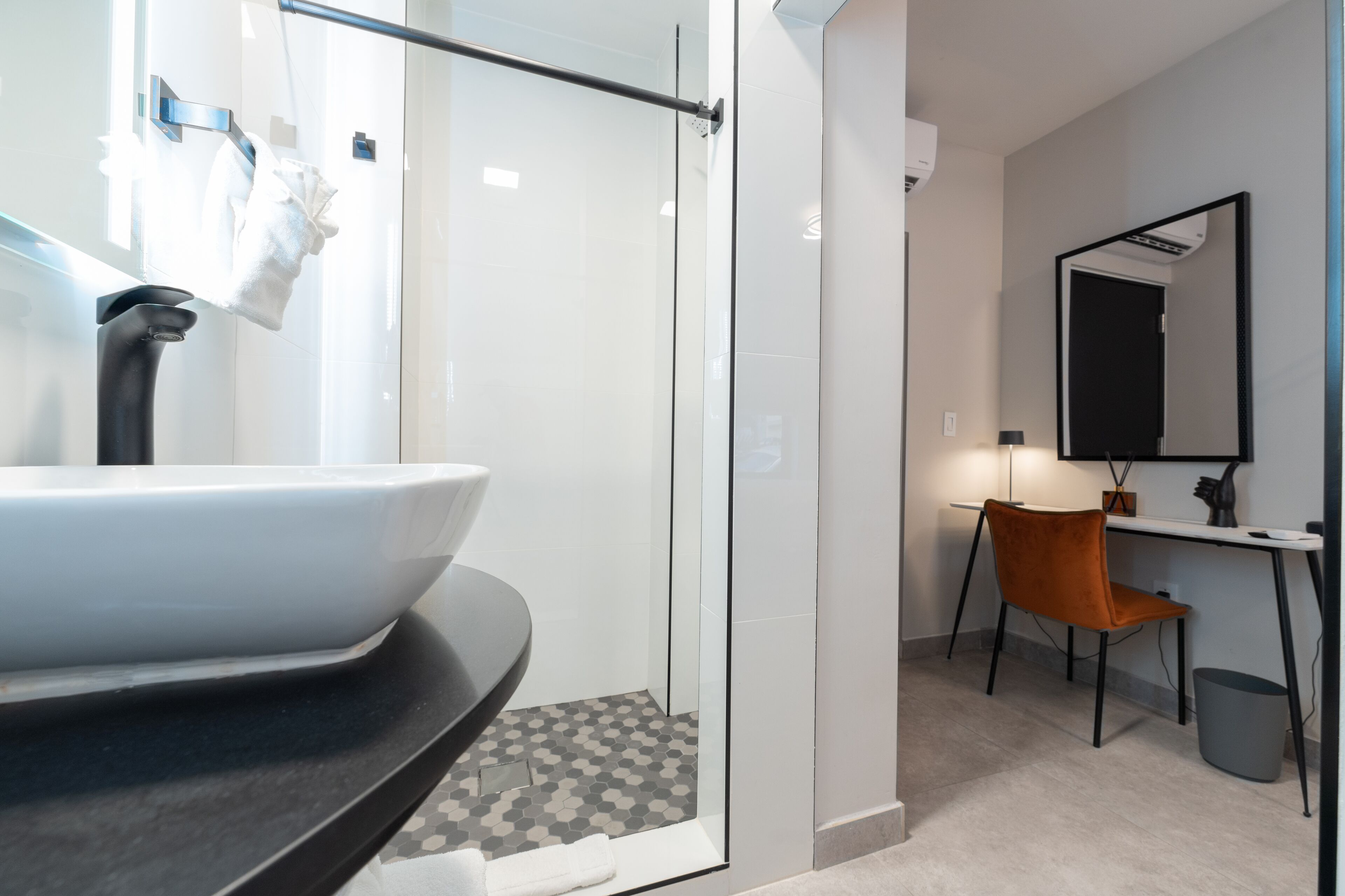 Un baño moderno con cabina de ducha de vidrio, lavabo blanco y escritorio con silla.