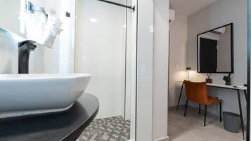 Un baño moderno con cabina de ducha de vidrio, lavabo blanco y escritorio con silla.