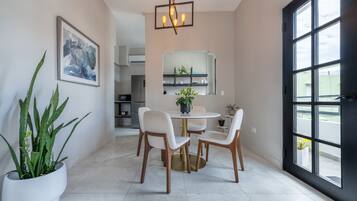 A dining area with a round table, four chairs, a potted plant, a framed abstract painting, and a modern chandelier.