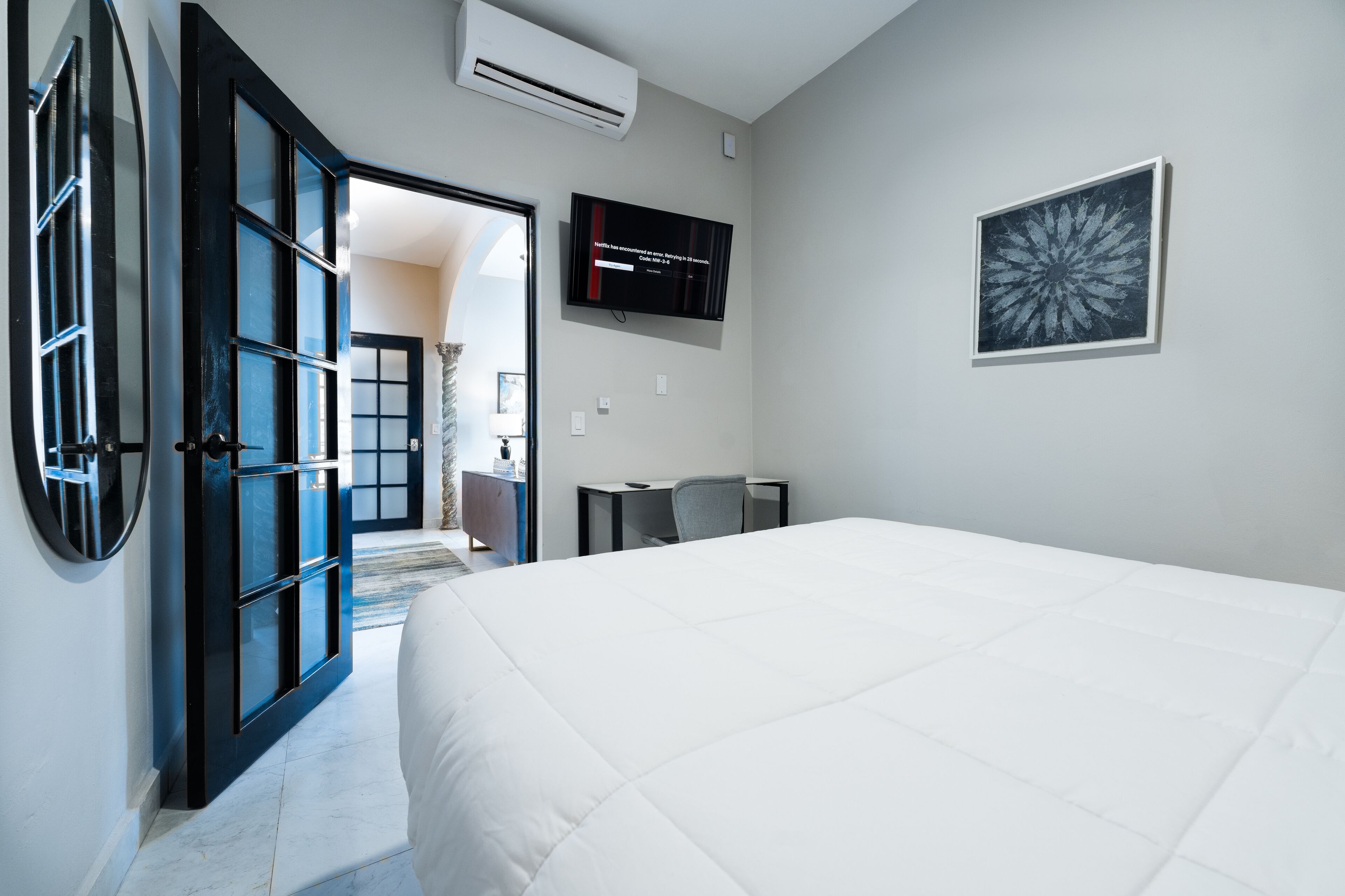 A hotel room with a large bed, a desk, a chair, a TV, and a door leading to another room.