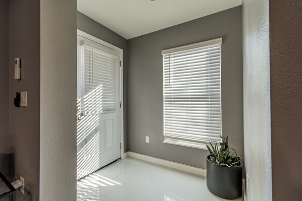 A hallway with a door, a window with blinds, and a potted plant.