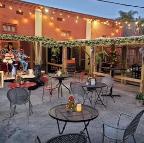Guests can dine al fresco at this outdoor patio area, featuring round tables and chairs, a stage with live music, and a festive atmosphere.