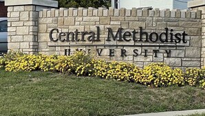 Eine Steinmauer mit der Aufschrift "Central Methodist University" und eine Reihe gelber Blumen im Vordergrund.
