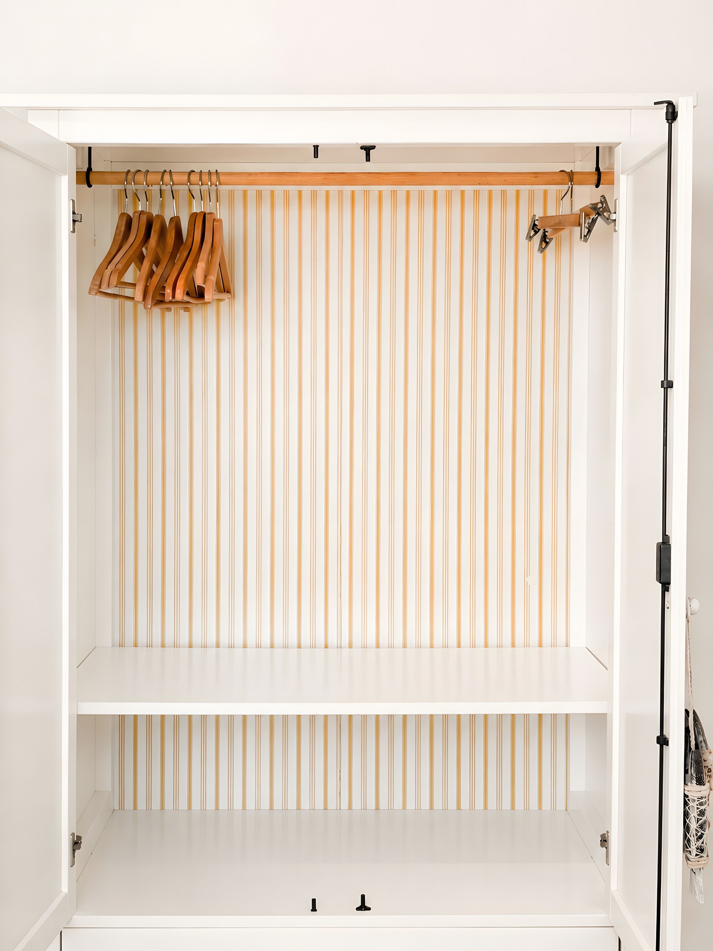 A white wardrobe with a striped back panel and wooden hangers.