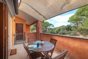 Un balcón con mesa y sillas, una puerta y vistas a árboles y colinas.