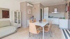 Une cuisine moderne avec des meubles blancs, une table à manger entourée de chaises en osier et un four à micro-ondes encastré.