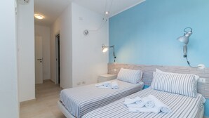 Une chambre d’hôtel avec deux lits, un mur d’accent bleu, une lampe moderne et un appareil de climatisation fixé au plafond.