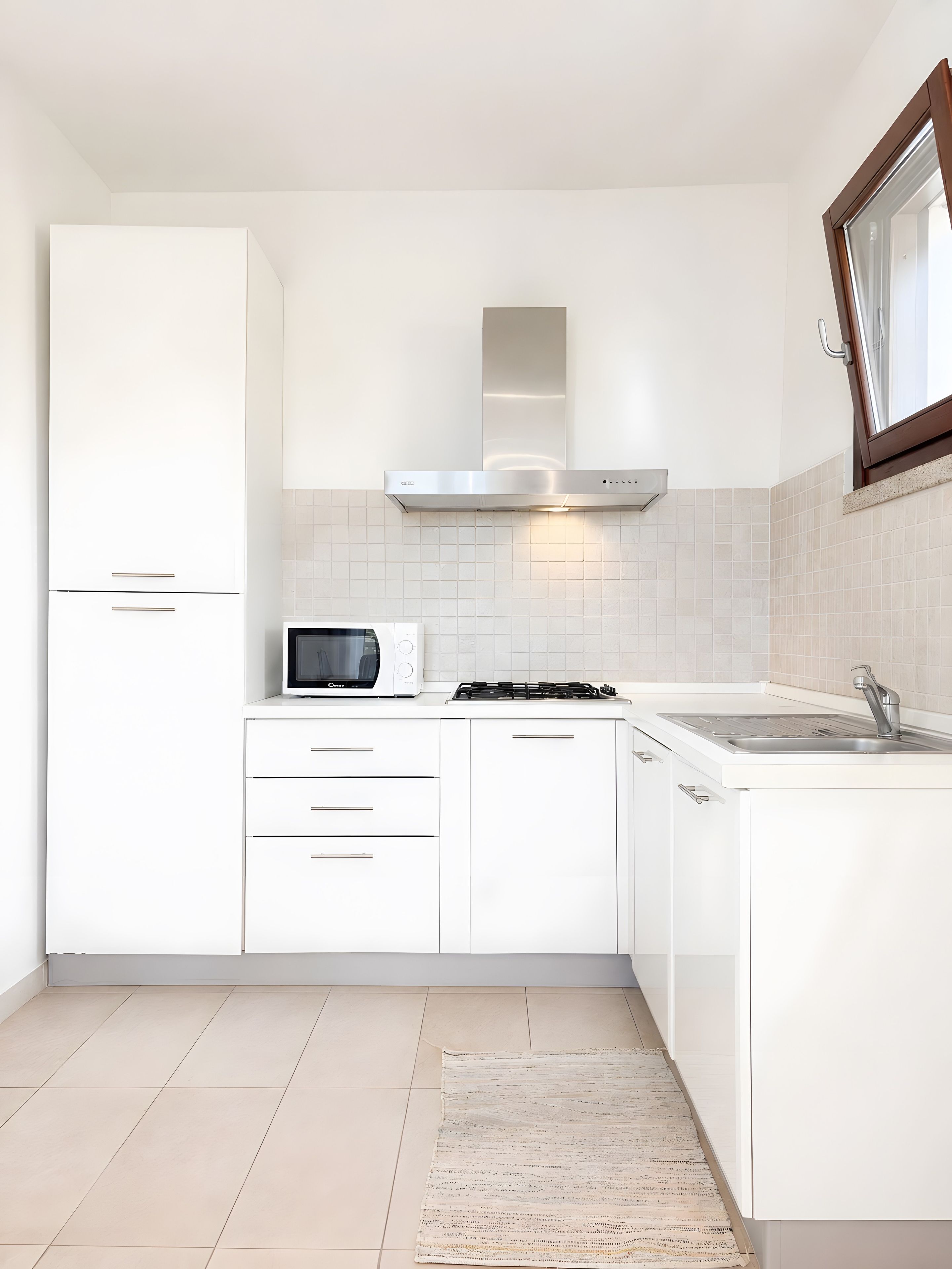 Una cucina moderna con mobili bianchi, forno a microonde integrato, piano cottura a gas e cappa aspirante in acciaio inossidabile.