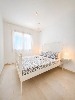 A bedroom with a bed, a nightstand, a window with curtains, and a ceiling light fixture.