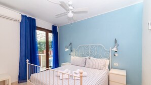 Camera da letto con un letto, comodini, una ventola a soffitto e vista attraverso una finestra con tende blu.